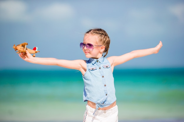 하얀 모래 해변에 손에 장난감 비행기와 함께 행복 한 어린 소녀.