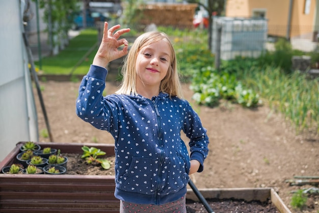 Счастливая маленькая девочка, работающая в огороде, показывает отличный жест пальцем
