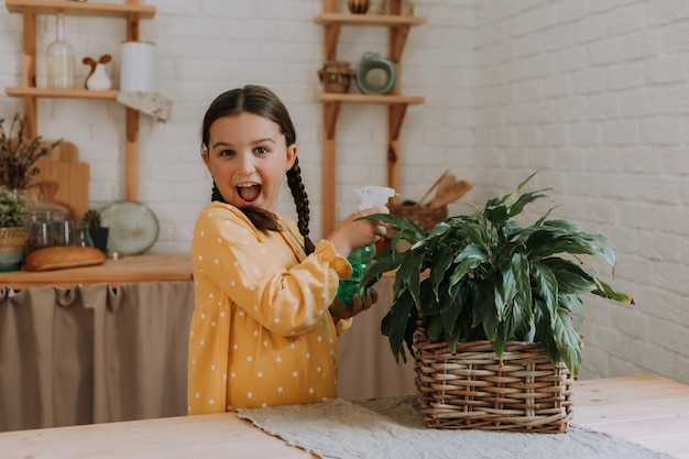 happy little girl in a yellow cotton dress is watering flowers at the dacha. wooden veranda