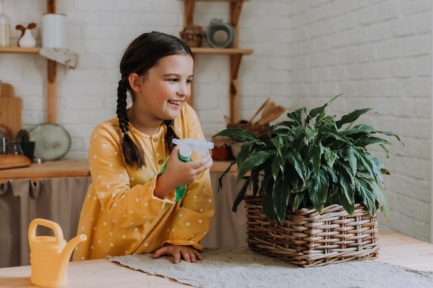 happy little girl in a yellow cotton dress is watering flowers at the dacha. wooden veranda