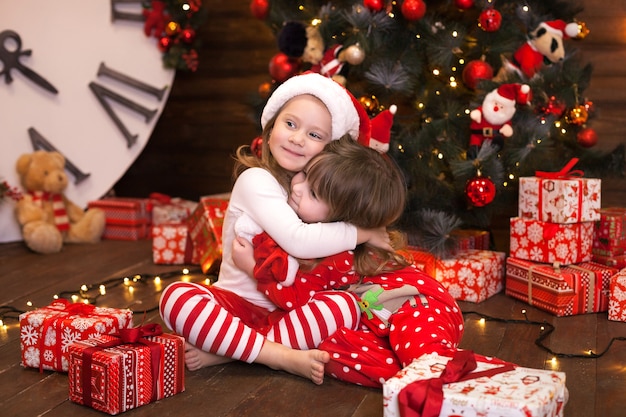 Happy little girls in red pajamas decorate a Christmas tree in living room