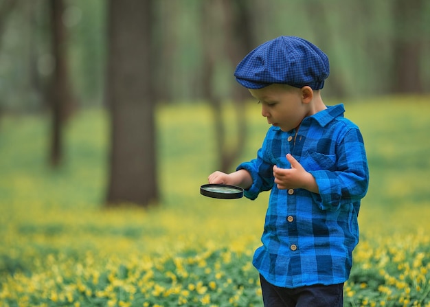 Happy little happy child boy exploring nature with magnifying glass summer concept of kid and nature