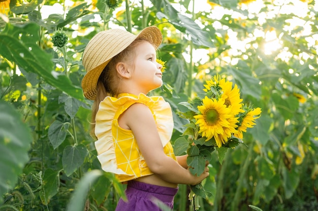 晴れた夏の日に咲くひまわり畑で遊ぶ麦わら帽子の幸せな小さな子供の女の子