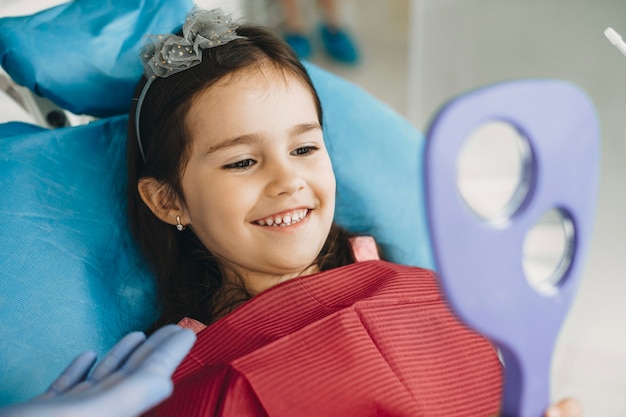 Photo happy little kid looking in the mirror after teeth examination in a pediatric stomatology.