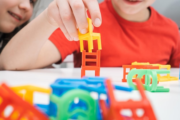 Happy little kids play toy colorful chairs sitting at table closeup Boy and girl build from small plastic furniture