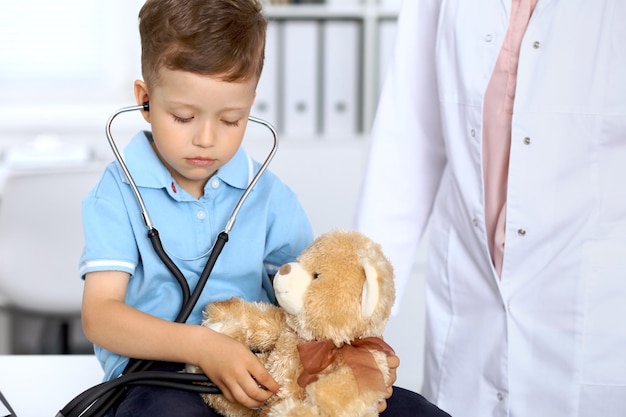 Happy little patient after health exam little doctor examining\
a toy bear with stethoscop