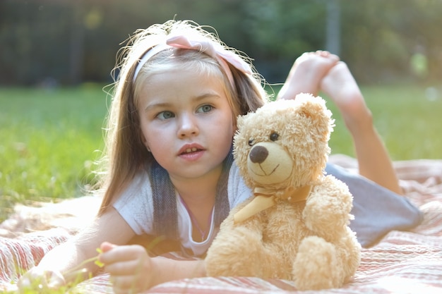 Photo happy little preeschool girl playing with her favorite teddy bear toy outdoors in summer park.