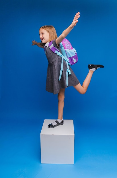 A happy little schoolgirl stands on a white cube on a blue background