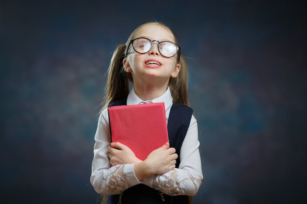 制服を着た幸せな小さな女子高生はタイトな本を保持します