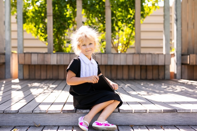 Happy little schoolgirl with lunch, book and pencils. Back to school outdoor