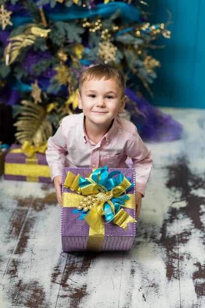 Il piccolo ragazzo sorridente felice tiene il contenitore di regalo di natale