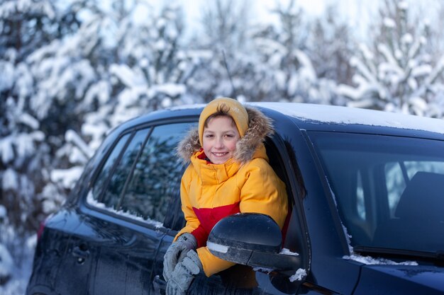 Happy little smilling boy look from a car window on a sunny day at winter snowy forest.