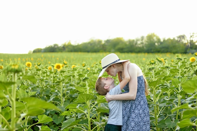 咲くひまわりのフィールドに立っている妊娠中の母親にキス幸せな幼い息子