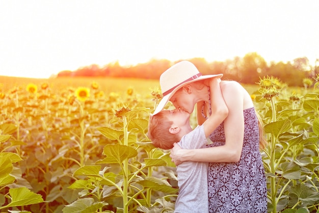 Piccolo figlio felice che bacia la madre incinta che sta sul campo soleggiato dei girasoli di fioritura. avvicinamento.