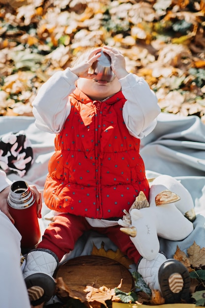 秋の自然の中で秋のピクニックで赤い魔法瓶とカップで幸せな小さな幼児赤ちゃん娘