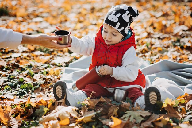 Photo happy little toddler baby daughter with red thermos and cup in autumn picnic in fall nature