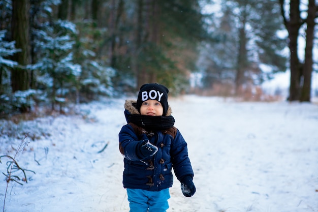 Piccolo ragazzo felice del bambino chiedendo i fiocchi di neve nella foresta di inverno