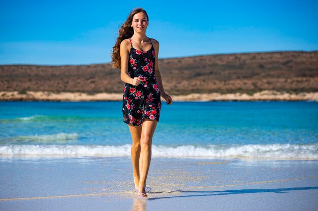 검은 드레스를 입은 행복한 장발 소녀가 호주 서부 청록색 만에 있는 물에 다리를 담근다