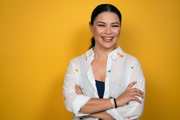 Happy looking Asian woman looks in camera, has toothy smile, wears casual clothing and arms folded