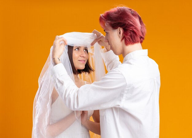 Happy looking wedding couple groom and bride in wedding dress under veil, groom taking firts look at his bride