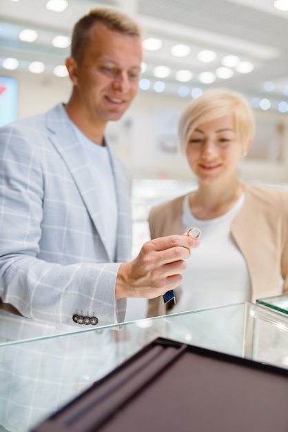 宝石店で結婚指輪を選ぶ幸せな愛のカップル。男と女の金の装飾を選択します。ジュエリーショップでの新郎新婦