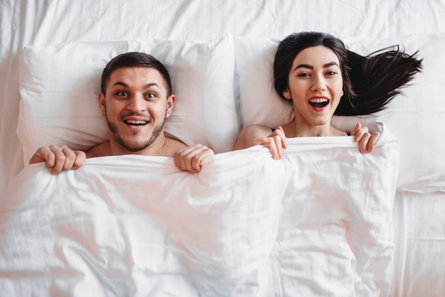 Coppie felici di amore si trovano sul grande letto bianco, vista dall'alto. partner intimi sorridenti in camera da letto, amanti dell'intimità calda