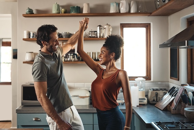 Happy in love and dancing while an interracial couple have fun and enjoying time together in home kitchen Husband and wife sharing a dance while being active and affectionate in loving relationship