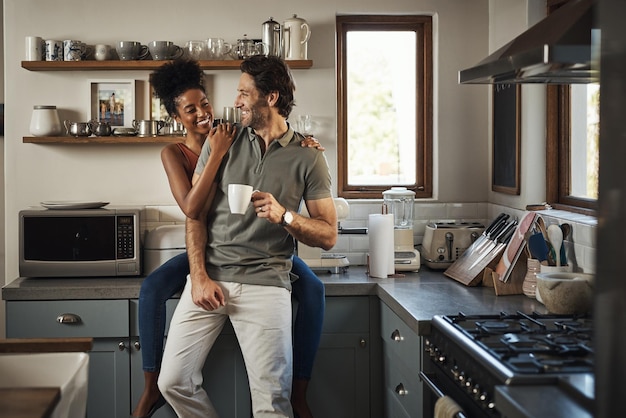 Photo happy in love and laughing while an interracial couple enjoys morning coffee and bonding while having good communication in a relationship husband and wife talking while standing in kitchen at home