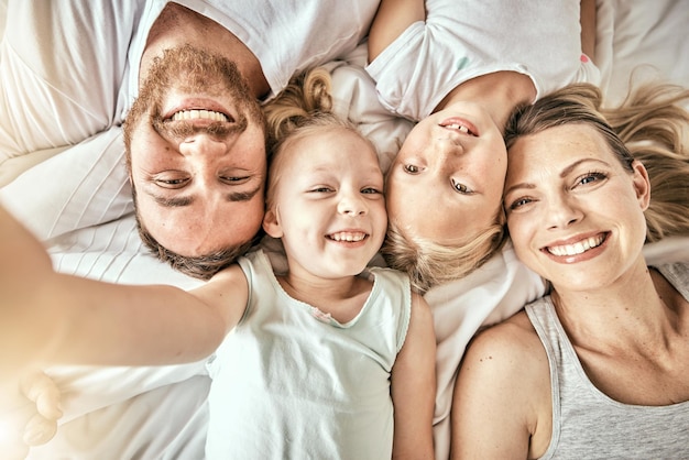 Foto amore felice e ritratto di famiglia su un letto per legare e rilassarsi insieme in una casa moderna sorriso di felicità e vista dall'alto di bambine sdraiate con i genitori australiani nella camera da letto di casa