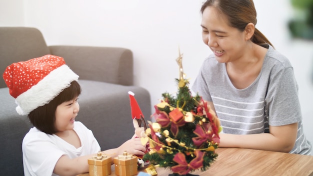 Happy lovely Asian girl decorating ornament on Christmas tree with her mother