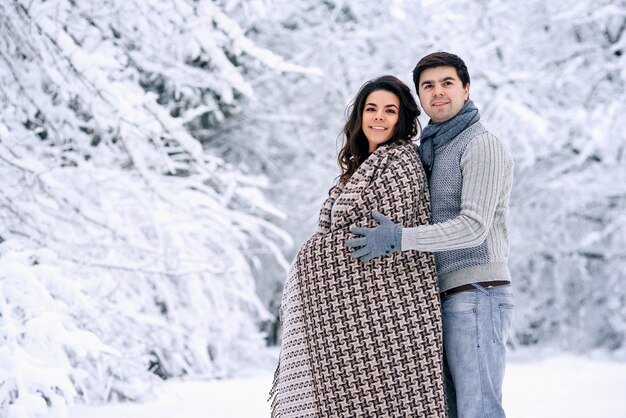 Happy lovely couple covered with a warm blanket and walking in a snowy park