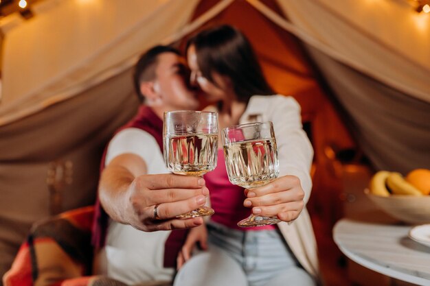 Happy lovely couple relaxing in glamping on summer evening and drinking wine near cozy bonfire Luxury camping tent for outdoor recreation and recreation Lifestyle concept