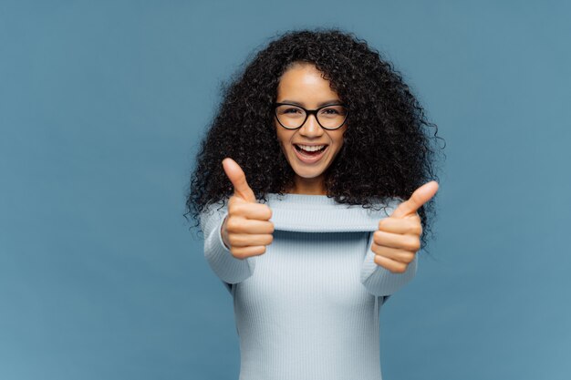 Happy lovely woman with bushy Afro hair gives thumb up, approves nice idea