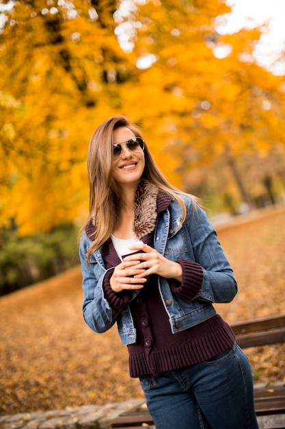 秋の公園で屋外のコーヒーを飲んで幸せな素敵な若い女性