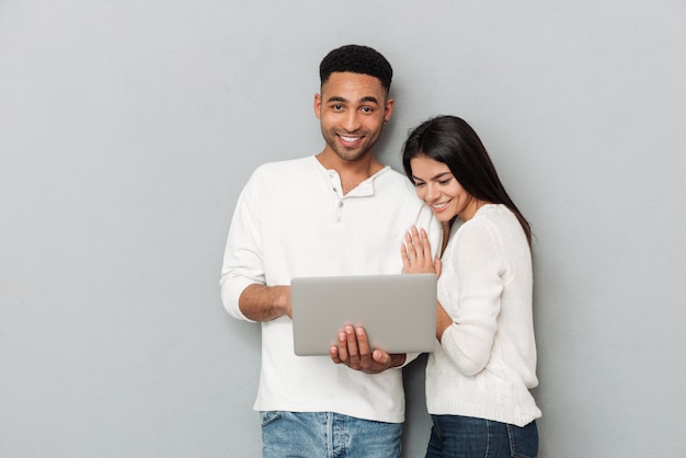 Happy loving couple over grey wall chatting by laptop