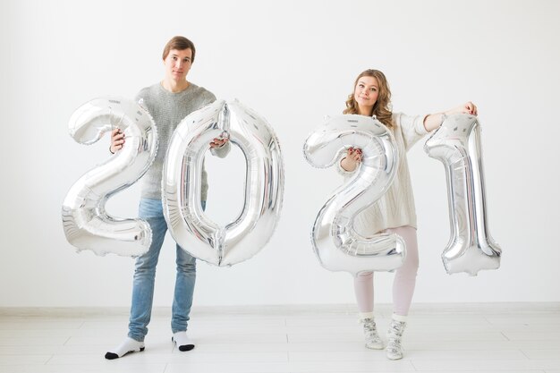 A happy loving couple holds silver 2021 balloons