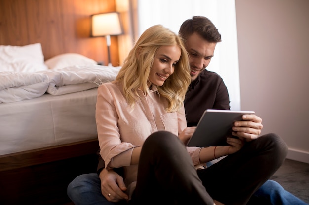 Happy loving couple sitting on the floor with digital tablet