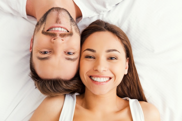 Happy loving couple. Top view of beautiful young loving couple lying in bed together and smiling