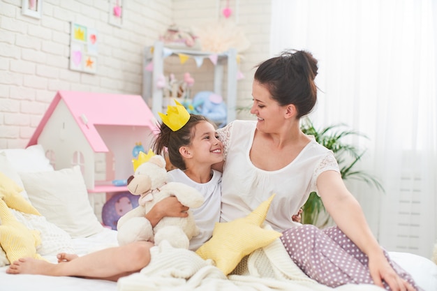 Happy loving family. ÃÂÃÂÃÂÃÂÃÂÃÂÃÂÃÂ¾ÃÂÃÂÃÂÃÂ¼ and daughter play in crowns and cuddle on bed.