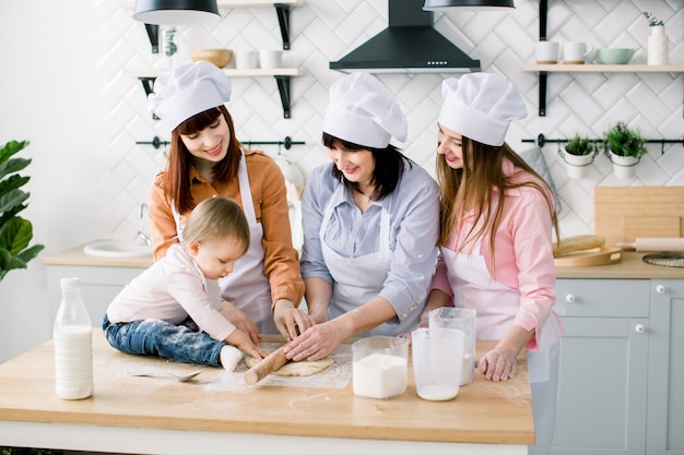 Happy loving family are preparing bakery together. Grandmother, two daughters and child granddaughter girl are baking cookies and having fun in the kitchen. Homemade food and little helper.