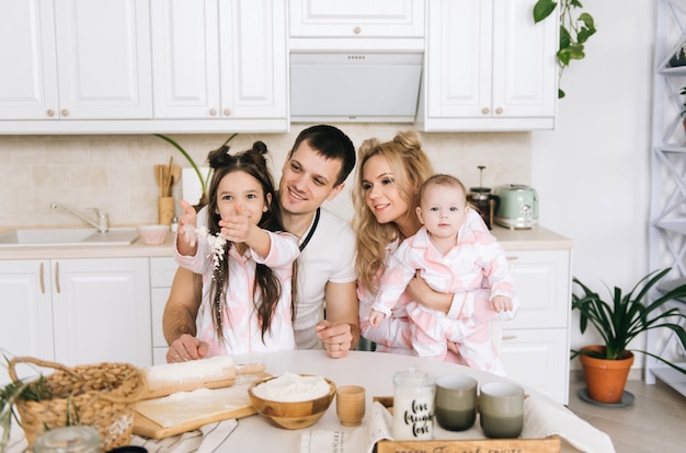 Happy loving family are preparing bakery together. Mother father  and two daughter girl are cooking cookies and having fun in the kitchen. Homemade food and little helper.