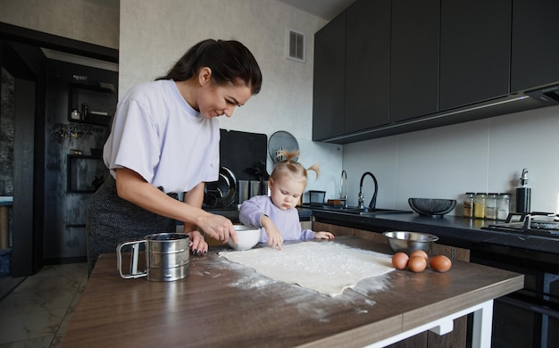Счастливая любящая семья вместе готовить пекарню. Мать и дочка-девочка готовят печенье и веселятся на кухне. Домашняя еда и маленький помощник.