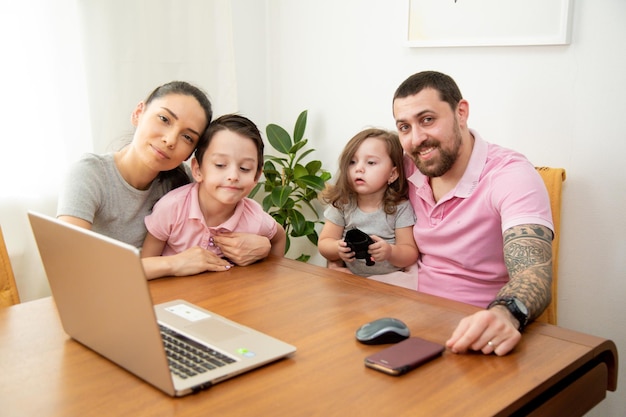 Famiglia amorevole felice coppia genitori e bambini carini figlio e figlia che usano il computer portatile in soggiorno al tavolo godendosi trascorrere del tempo insieme riposando a casa