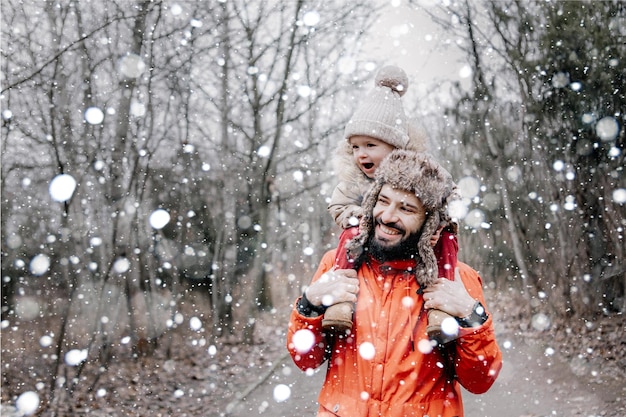 Happy loving family Father and his baby are playing and hugging outdoors Little child and daddy on snowy winter walk in nature Concept of the first longawaited winter snowfall