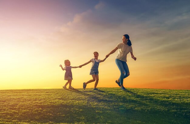 Happy loving family is having fun on nature in the summer Young mother and two daughters are laughing and playing on meadow at sunset background