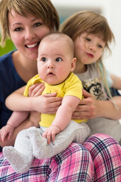 幸せな愛情のある家族。家で一緒に時間を過ごしている間、彼女の子供たちの小さな女の子と男の子がお互いを抱き締めている若い母親の肖像画