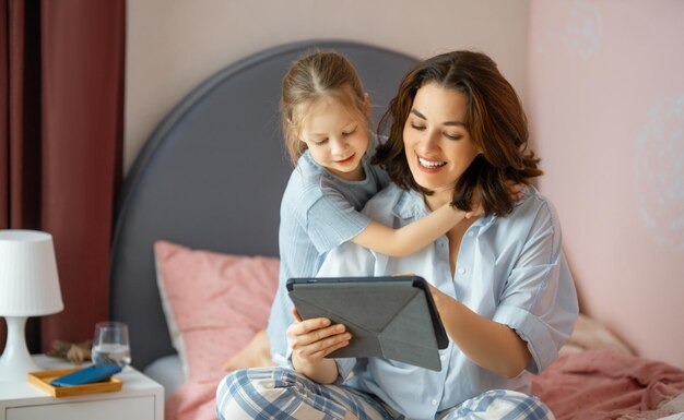 幸せな愛情のある家族。タブレットPCを使用して若い母と娘の女の子。面白いお母さんと素敵な子供が家で楽しんでいます。