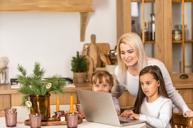 Счастливая любящая семья. Молодая мать и дочери девушки с помощью ноутбука. Веселая мама и милые дети весело проводят время дома.