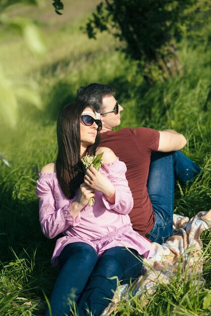 Happy loving young couple spending time in the park sitting on a green lawn on a sunny summer day