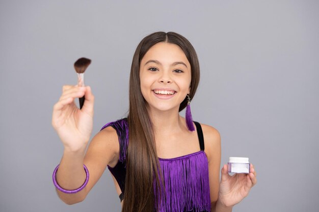 Happy makeup girl apply face powder with brush grey background makeup artist selective focus